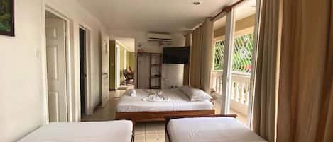 A hotel room with two single beds, a TV, and a balcony with curtains.