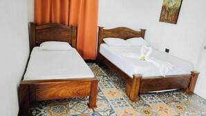 Two wooden beds with white linens, a patterned floor, and a single orange curtain. - Hotel Manglares (Caldera)