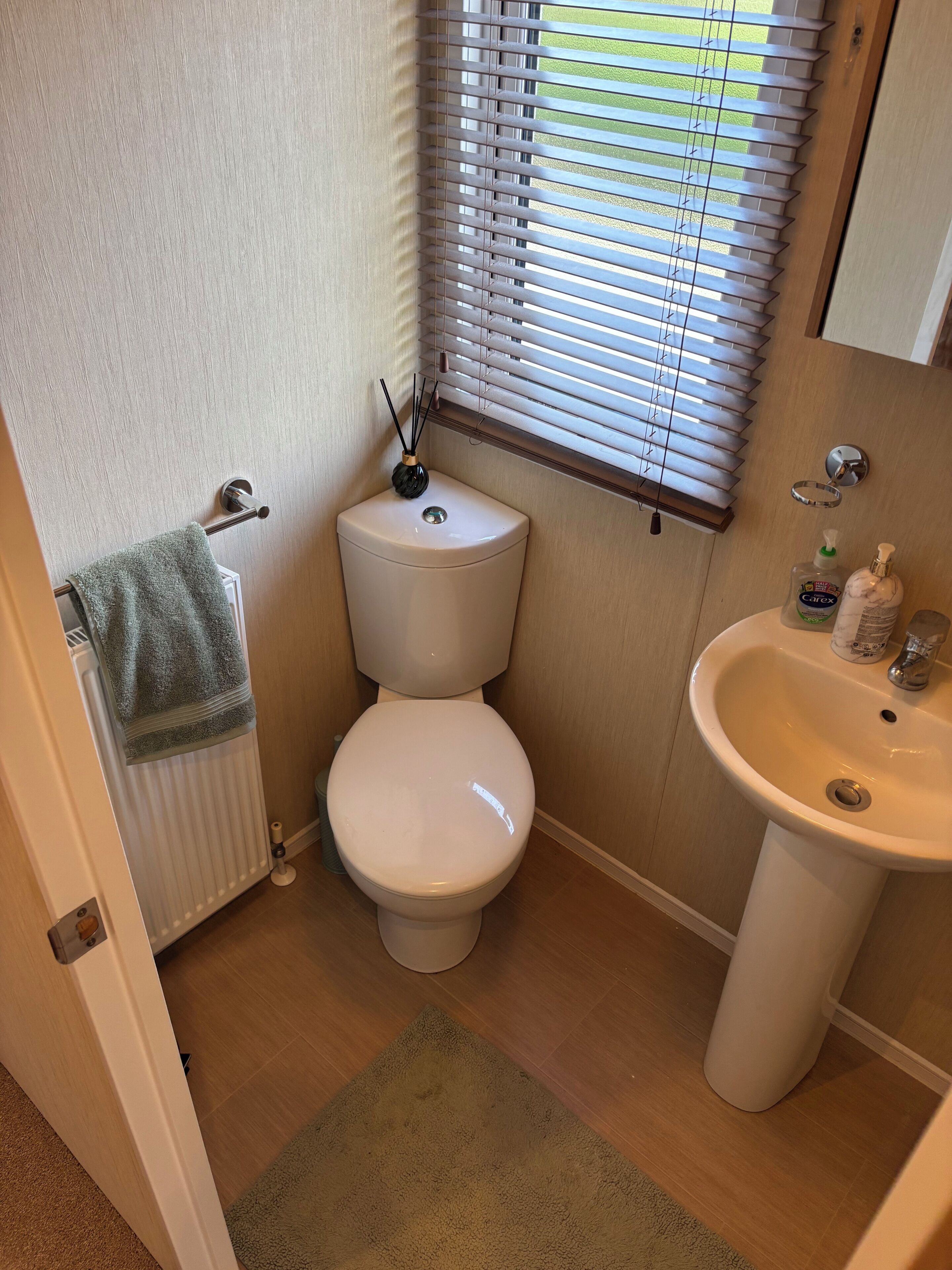 A bathroom with a toilet, a sink, a towel rack, and a window with blinds.