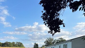 Ein Kiesweg führt zu einem hellblauen Wohnmobil mit umzäunter Rasenfläche unter blauem Himmel.