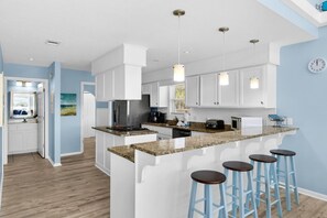 A modern kitchen with white cabinetry, granite countertops, and bar stools. - Sun and Sand (Panama City Beach)
