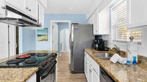 A modern kitchen with granite countertops, stainless steel appliances, and a view to the adjacent living area. - Sun and Sand (Panama City Beach)