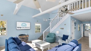 A spacious living room with a blue sofa set, a white coffee table, and a teal armchair. A staircase with a white railing leads to an upper level. - Sun and Sand (Panama City Beach)