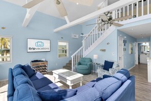 A spacious living room with a blue sofa set, a white coffee table, and a teal armchair. A staircase with a white railing leads to an upper level. - Sun and Sand (Panama City Beach)