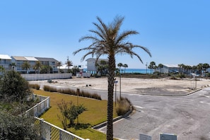 A beachfront property with a palm tree, a parking lot, and a building with a sign indicating it's an open house. - Sun and Sand (Panama City Beach)