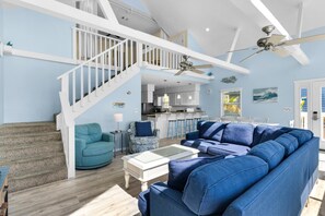 A spacious living area with a blue sofa, a teal armchair, and a white coffee table. A white staircase with a railing leads to an upper level. - Sun and Sand (Panama City Beach)