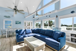 A spacious living room with a large blue sectional sofa, a glass coffee table, and a ceiling fan. - Sun and Sand (Panama City Beach)