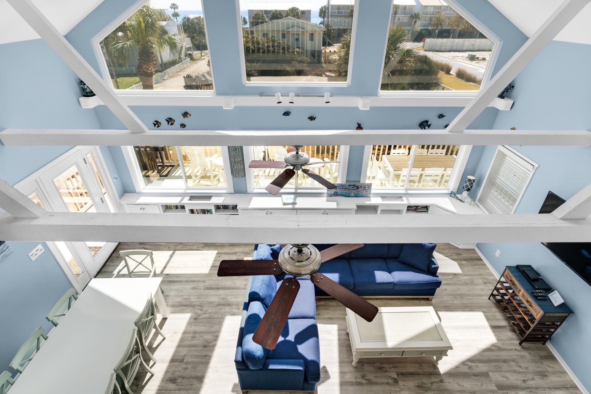 Ein geräumiger Raum mit hoher Decke, Deckenventilator, einem blauen Sofa und Blick ins Freie.