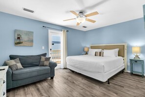 A hotel room with a bed, a sofa, a ceiling fan, and a painting on the wall. - Sun and Sand (Panama City Beach)