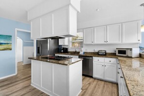 A modern kitchen with white cabinetry, granite countertops, stainless steel appliances, and a view of the outdoors. - Sun and Sand (Panama City Beach)