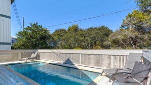 A rectangular swimming pool with a wooden deck and lounge chairs. - Sun and Sand (Panama City Beach)