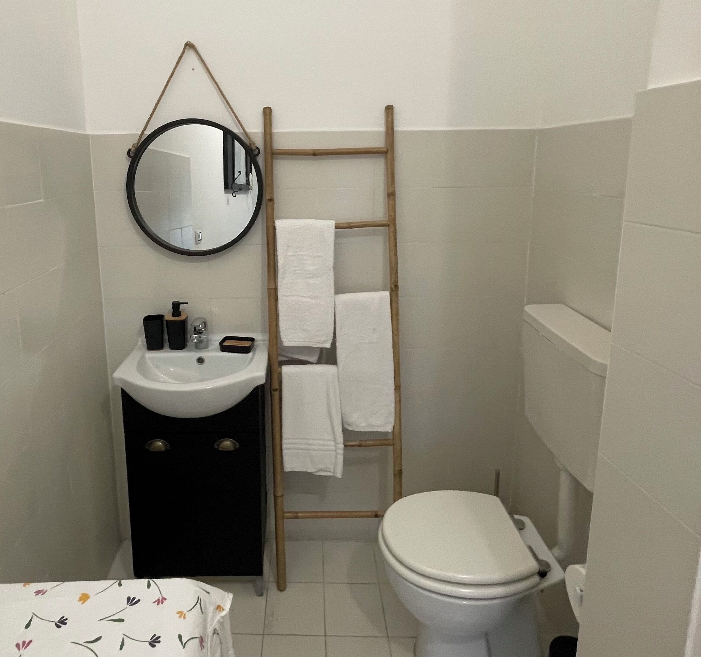 Un baño con lavamanos blanco, espejo y retrete. Hay una escalera de madera apoyada en la pared.