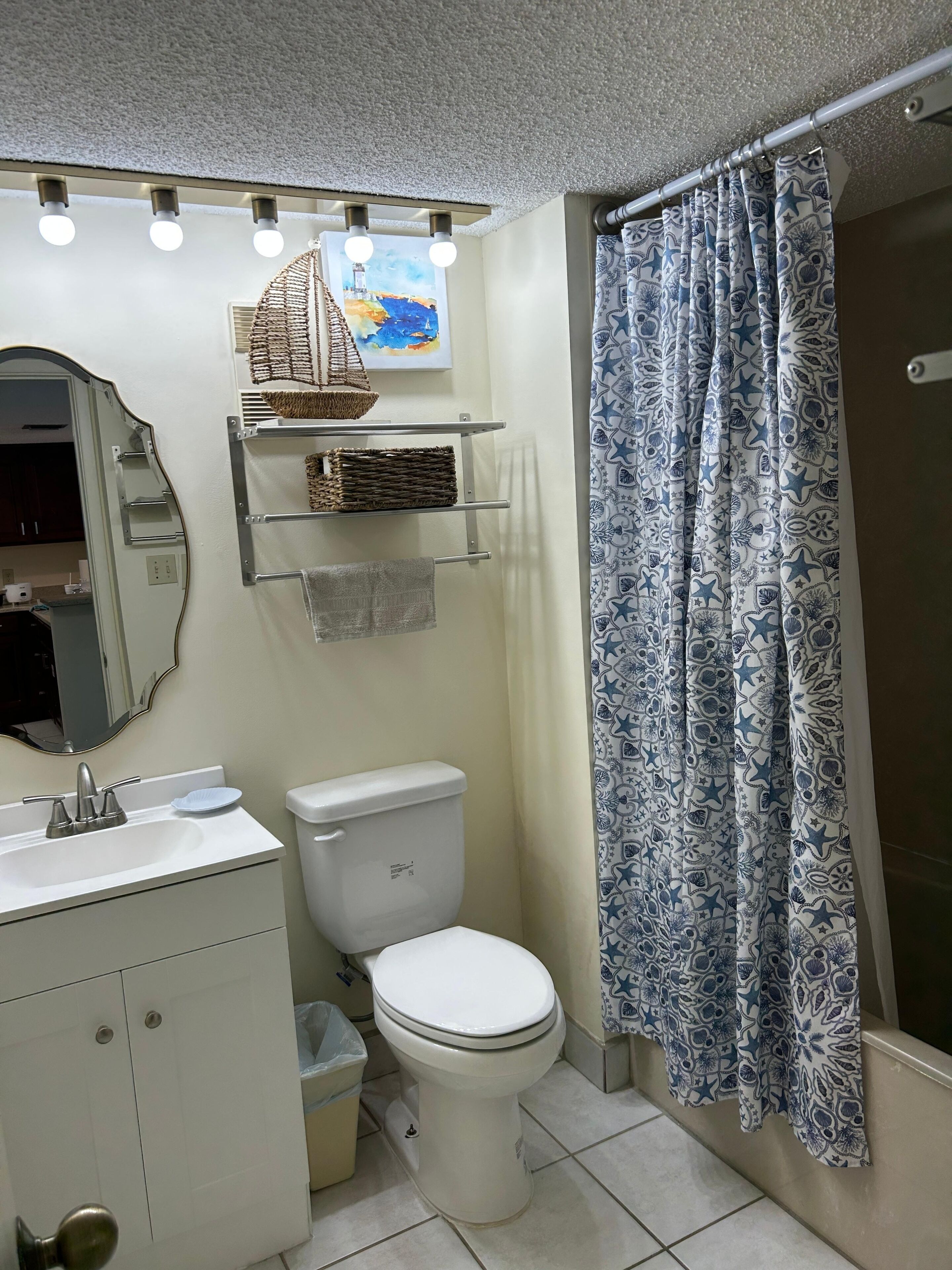A bathroom with a toilet, sink, mirror, and a shower curtain with a nautical pattern.