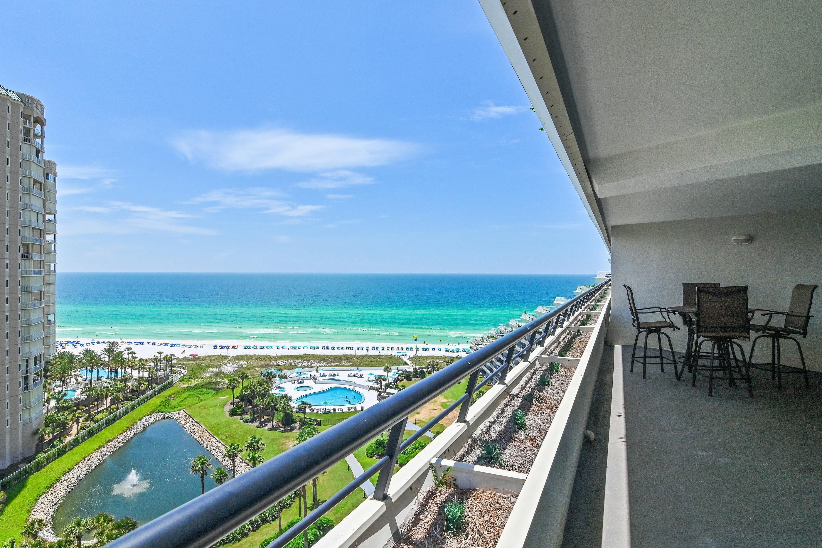 A balcony with a view of a beach, a pool, and a resort area.