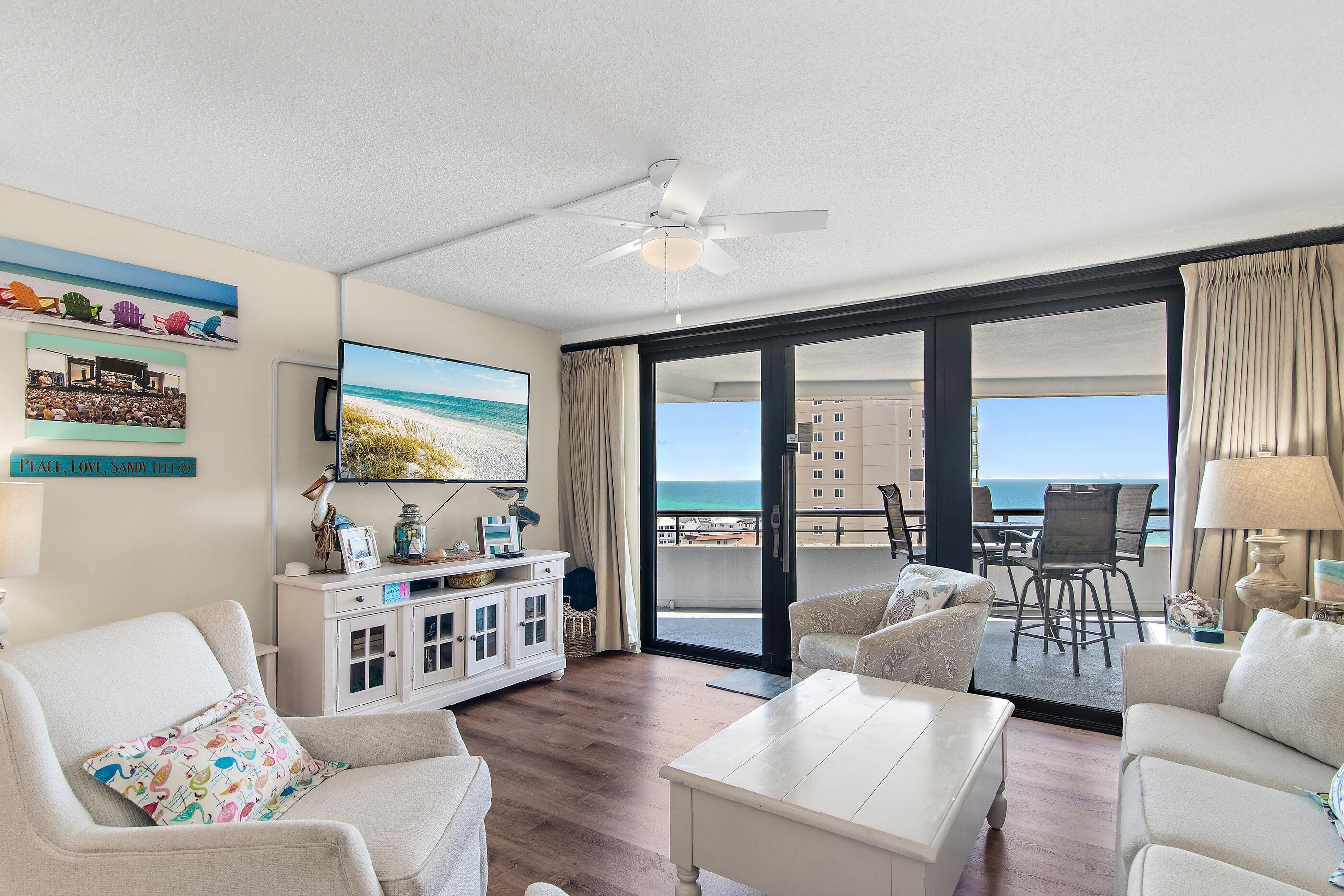 A living room with a television, a ceiling fan, and a view of the ocean through large sliding doors.