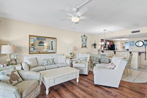 A living room with a ceiling fan, a dining area with a kitchen in the background, and a large mirror on the wall. - Edgewater #1400 - Emerald View (Miramar Beach)