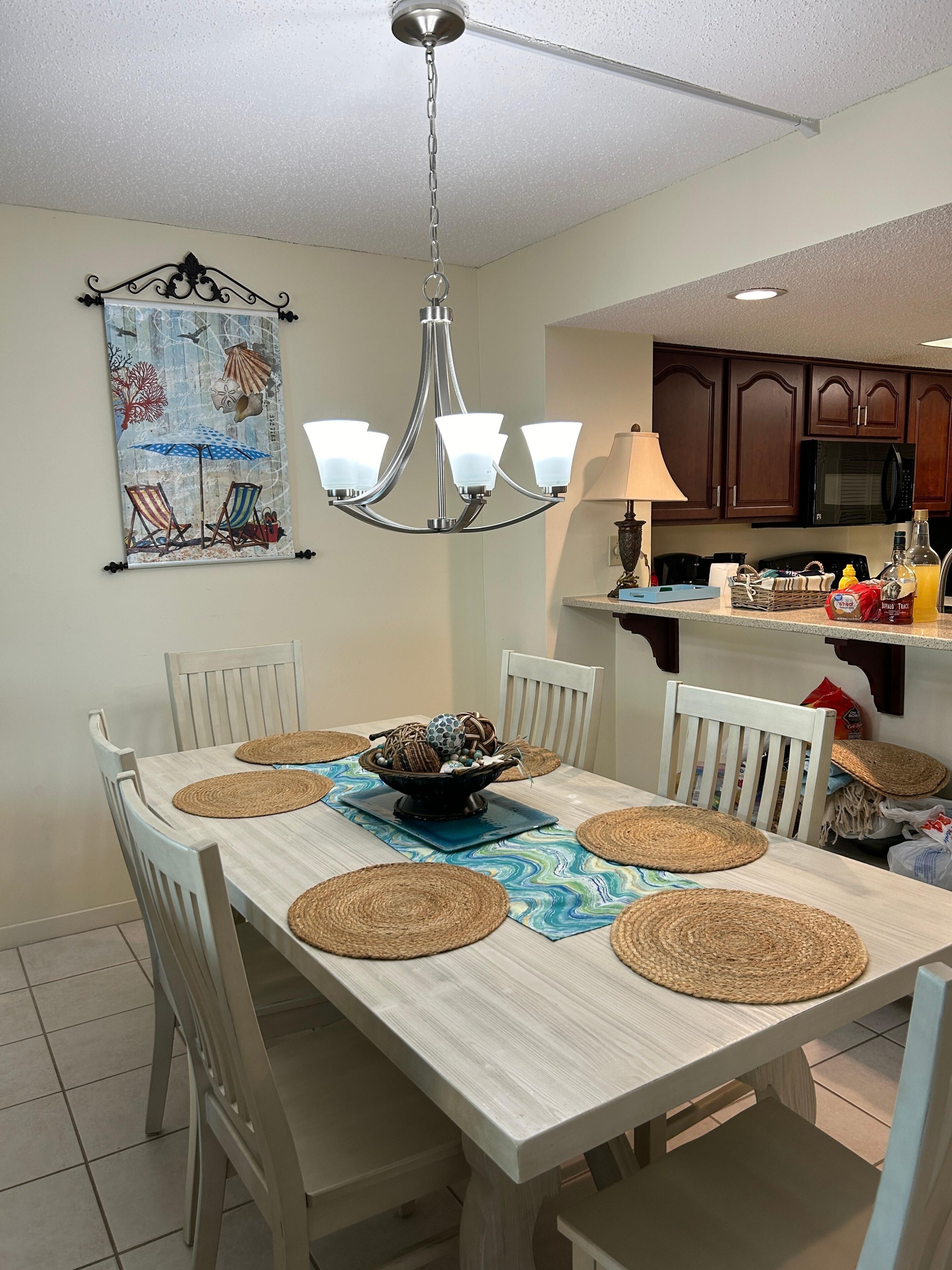 A dining area with a table set for four, surrounded by white chairs, a chandelier, and a wall-mounted artwork.