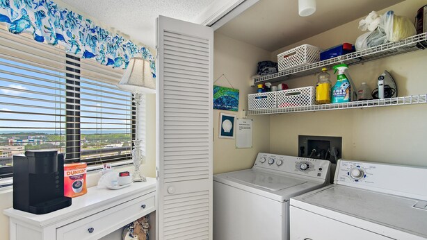 Ein Waschbereich mit Waschmaschine, Trockner und Regalen für Reinigungsmittel.