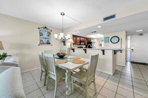 A dining area with a table set for four, a chandelier, and a kitchen in the background. - Edgewater #1400 - Emerald View (Miramar Beach)
