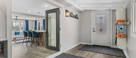 Un intérieur moderne avec un plancher en bois, une porte en verre donnant sur un coin repas et une porte blanche agrémentée d’un panneau de verre décoratif.
