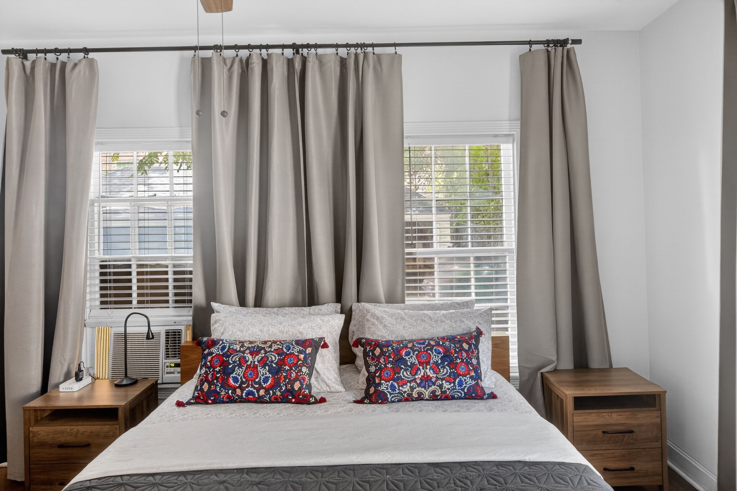 Ein Schlafzimmer mit einem Bett, zwei Nachttischen, einem Fenster mit Jalousien und Vorhängen.