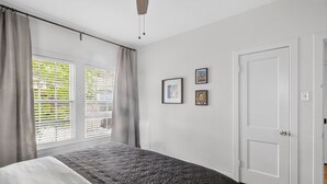 A bedroom with a bed, a window with blinds, a door, and two framed pictures on the wall. - Museum & Med District Retreat 2BR + Parking (Houston)