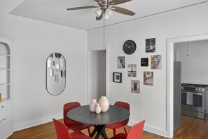 A modern kitchen with stainless steel appliances, a dining area with a round table and red chairs, and a hallway with framed pictures on the walls. - Museum & Med District Retreat 2BR + Parking (Houston)
