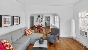 A modern living room with a grey sofa, a coffee table, and a dining area with a round table and chairs. - Museum & Med District Retreat 2BR + Parking (Houston)