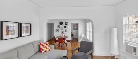A modern living room with a grey sofa, a coffee table, and a dining area with a round table and chairs.