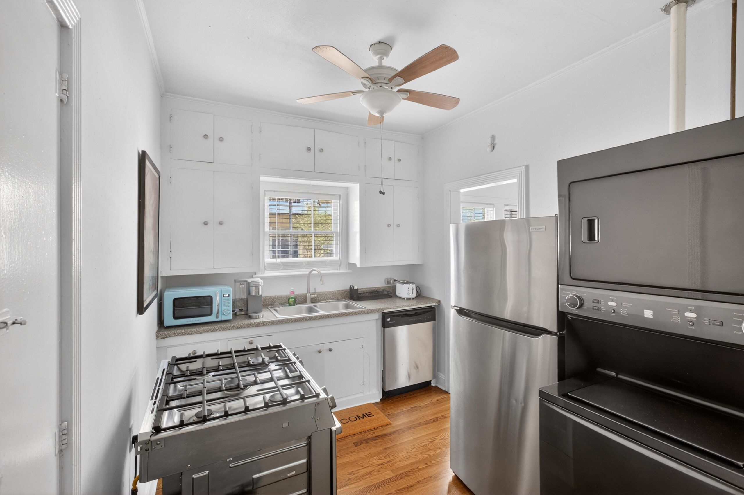 A compact kitchen with white cabinets, a gas stove, a stainless steel refrigerator, and a built-in oven.