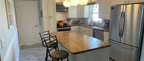 A modern kitchen with a central island, bar stools, stainless steel appliances, and pendant lighting.
