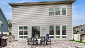 Ein zweistöckiges Haus mit einer Terrassenfläche, die einen Grill, einen Esstisch und Stühle bietet.