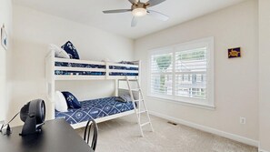 Ein Zimmer mit Etagenbetten, einem Schreibtisch, einem Stuhl, einem Ventilator und einem Fenster mit Jalousien.