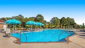 Ein Schwimmbecken mit mehreren Liegestühlen und Sonnenschirmen, umgeben von Bäumen.