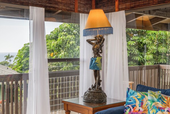 A room with a view of the ocean, a statue, a table, and a couch.