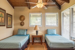 Ein Schlafzimmer mit zwei Betten, einem Deckenventilator und Fenstern mit Jalousien.