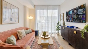 A living room with a sofa, coffee table, and a TV wall art display. - 1BR 1BA Miami Apt Pool Ocean Views Ideal for 3 (Miami)