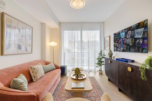 A living room with a sofa, coffee table, and a TV wall art display. - 1BR 1BA Miami Apt Pool Ocean Views Ideal for 3 (Miami)