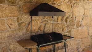 Ein tragbarer Grill mit Metallgestell und Rädern, vor einer Steinmauer platziert.