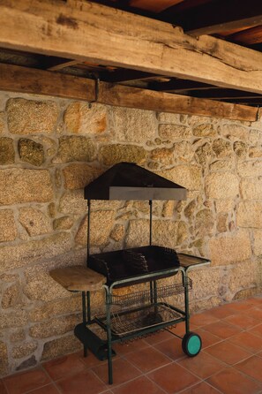 Ein tragbarer Grill mit Metallgestell und Rädern, vor einer Steinmauer platziert.