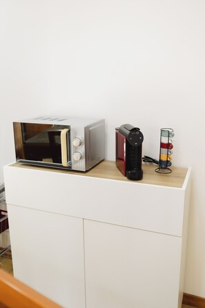 A microwave on a white cabinet with a coffee maker and a red appliance on top. - COUTO REFUGE (Cabeceiras de Basto)