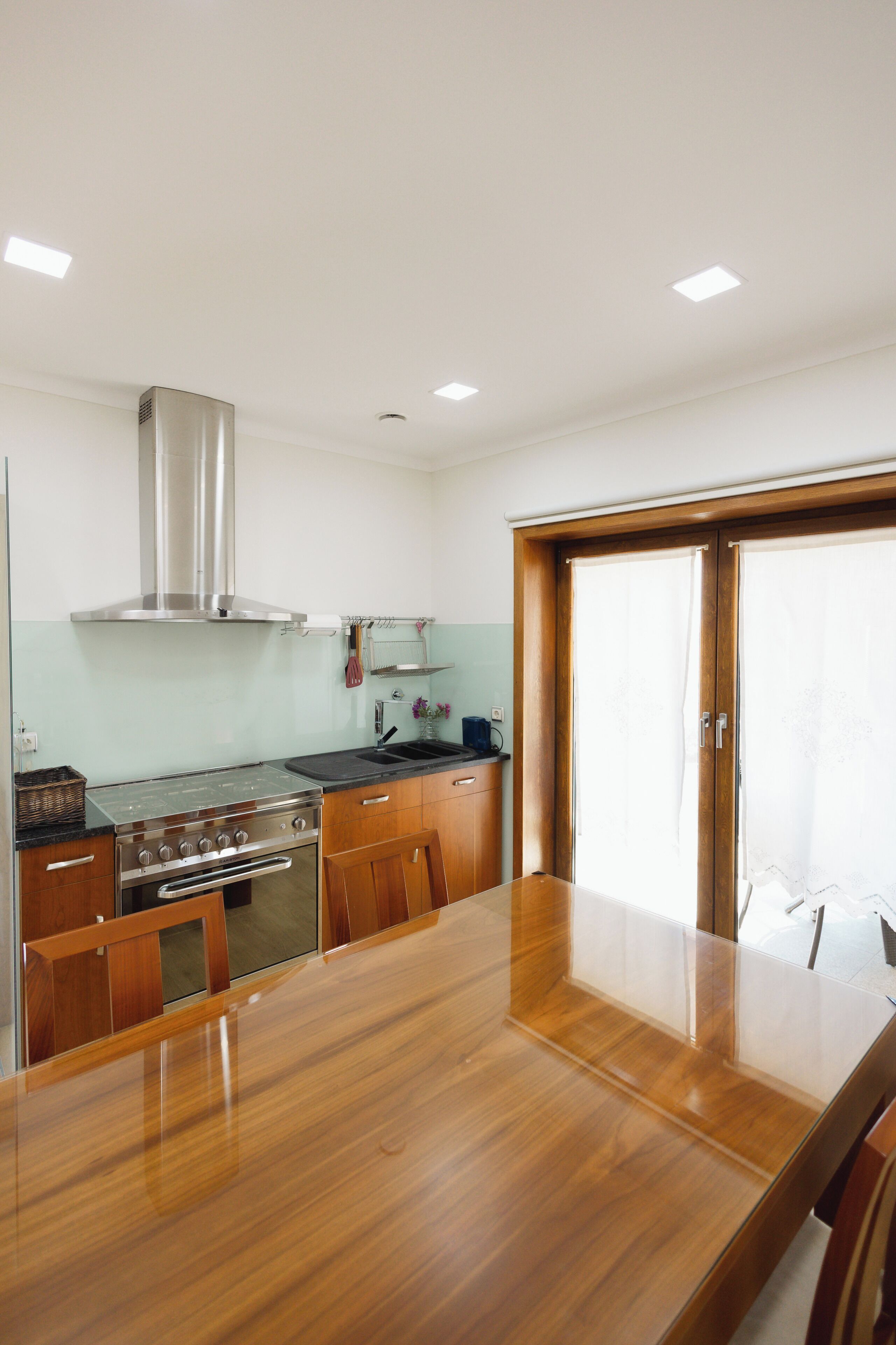 A modern kitchen with a stainless steel stove, wooden cabinets, and a large dining table.