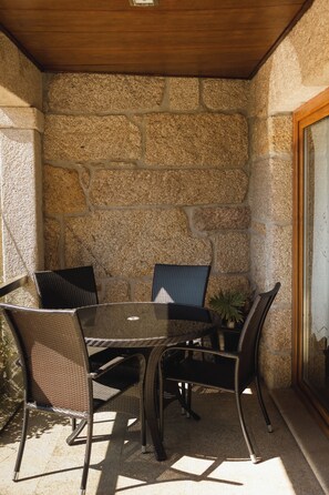 Een terras buiten, met een stenen muur, een tafel en vier stoelen.