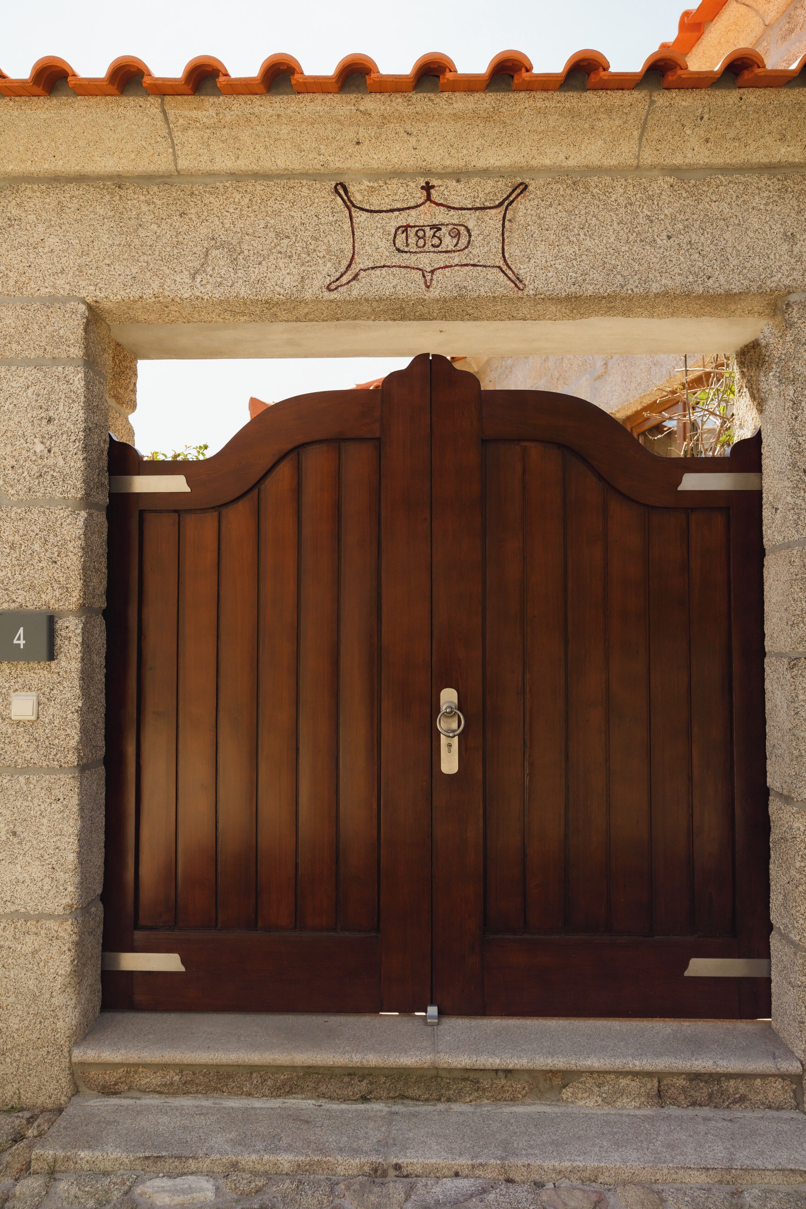 Une grande porte en bois, munie d’un cadenas en métal, est encadrée par une arche en pierre sur laquelle est fixée une plaque.