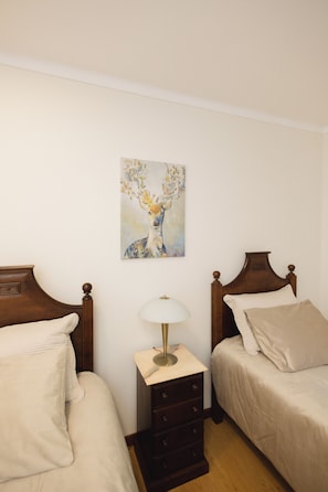 A bedroom with two beds, a nightstand, a lamp, and a painting on the wall. - COUTO REFUGE (Cabeceiras de Basto)