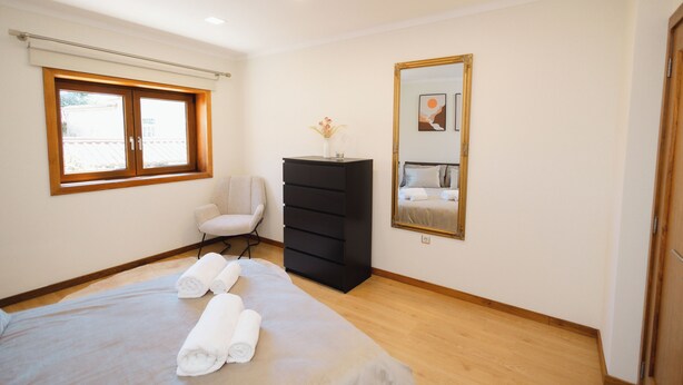 Ein Schlafzimmer mit Bett, Stuhl, Kommode, Fenster und Spiegel.