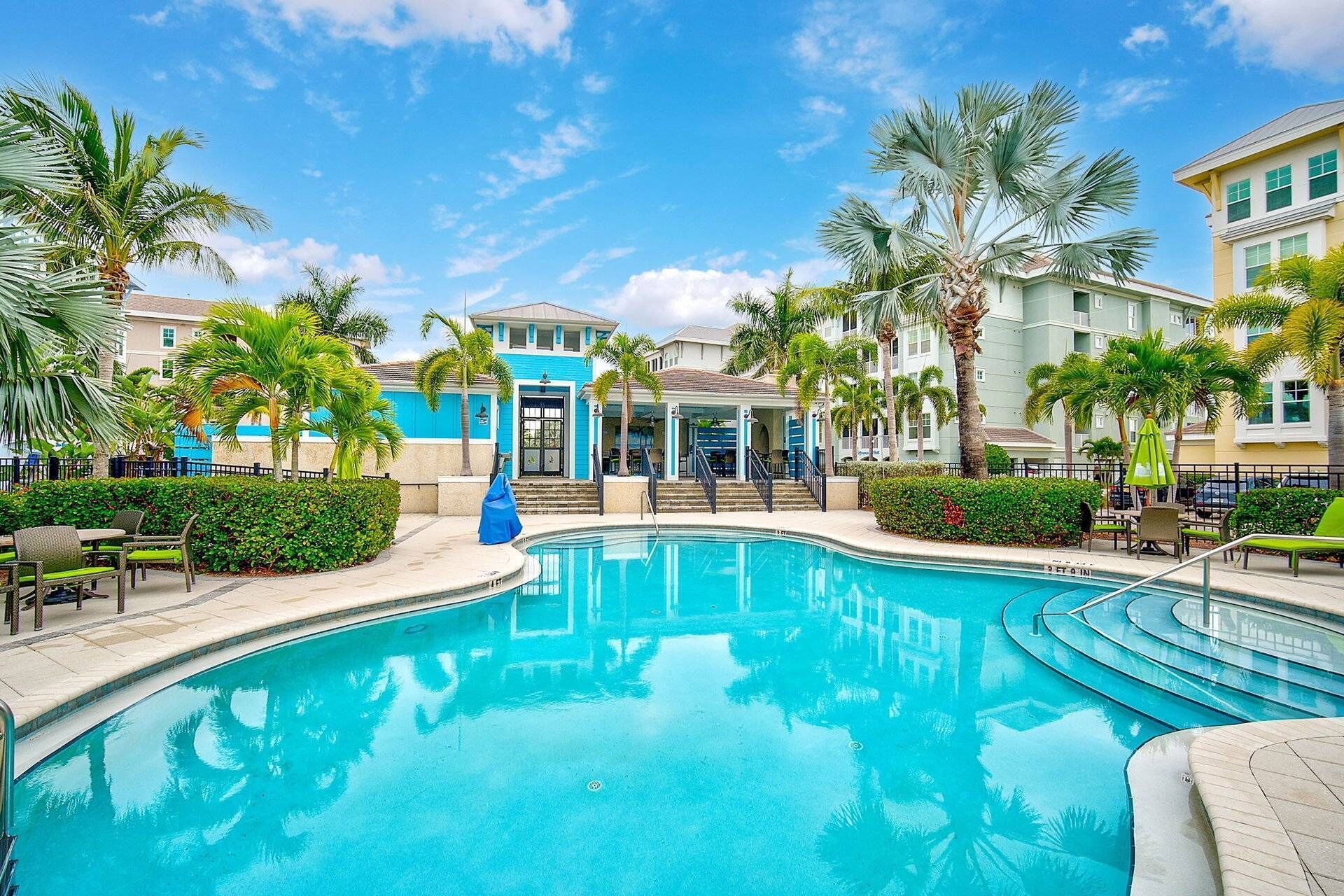 A swimming pool with a clear blue water surface, surrounded by palm trees and a building with a blue facade.