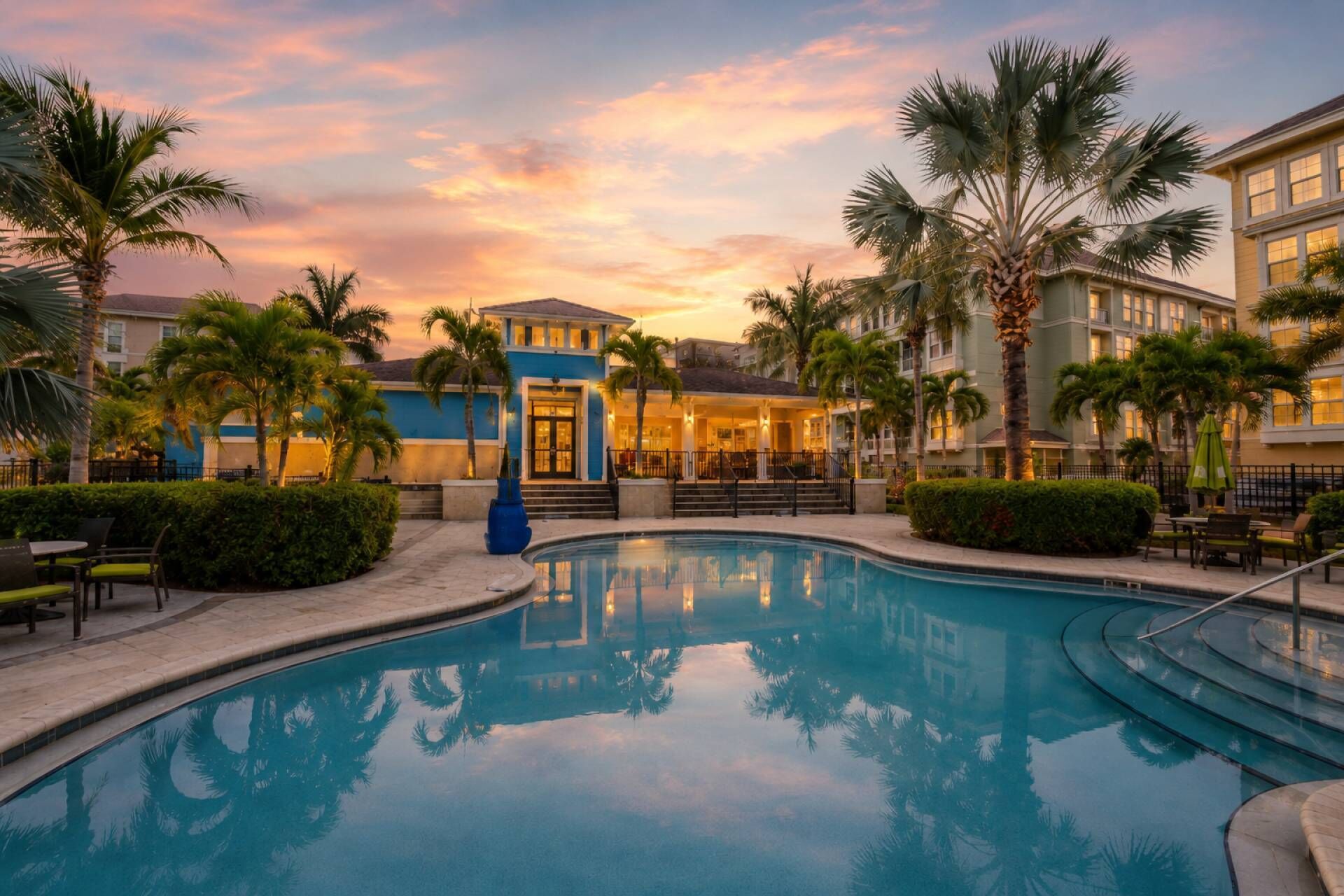 A resort pool area with a clear view of the pool, palm trees, and a building with a balcony.