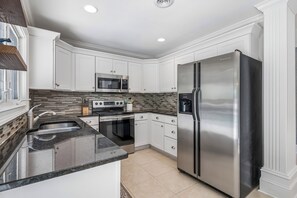 Una cocina moderna con armarios blancos, un refrigerador de acero inoxidable, un microondas y una estufa.