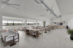 Ein großzügiger Wohnbereich mit einem großen Esstisch, verschiedenen Sitzgelegenheiten, Deckenventilatoren und einer Küche im Hintergrund.